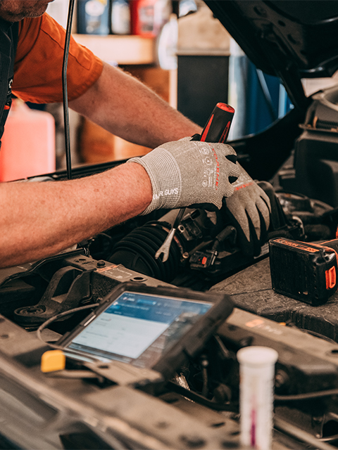 Mechanic working on a car engine with a diagnostic device nearby.