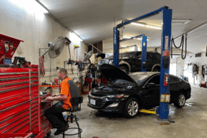 Vehicle inspection, auto repair in Belton, MO at Belton Transmission & Complete Auto Repair. Image of a technician working beside vehicles on service lifts, including a sedan with its hood open.