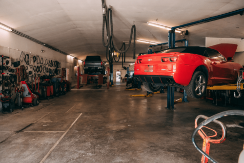 Interior view of Belton Transmission & Complete Auto Repair in Belton, MO, showing a red Chevrolet Camaro and another vehicle on hydraulic lifts, surrounded by tools.