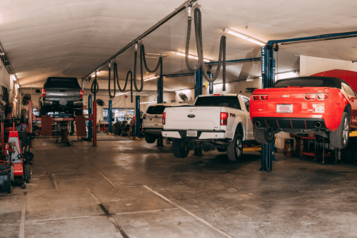 Image of spacious auto repair shop with multiple vehicles on hydraulic lifts, including trucks and a sports car, receiving professional maintenance and repair services in a clean service bay.