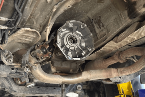 Transmission repair in Belton, MO by Belton Transmission & Complete Auto Repair. Image of a vehicle's undercarriage with the transmission housing exposed during a drivetrain repair, showing exhaust components and lift support arms in a professional shop.